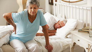 Older woman sitting on the edge of the bed with hip pain