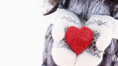 Woman in a winter scene, wearing gloves and holding a red heart in her hands