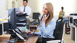 Young professional women taking a phone call at her desk in a busy office.