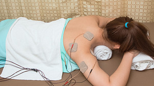 Woman lying prone with a TENS unit connected to the upper back.