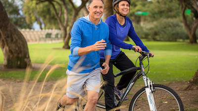 A woman riding a bicycle while a man runs along side her for exercise