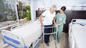 Older man being assisted by a physician to use his walker in the hospital