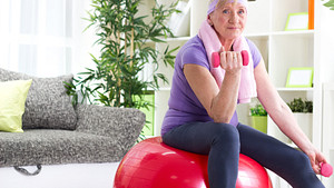 Older woman working out with dumbbells and an exercise ball.