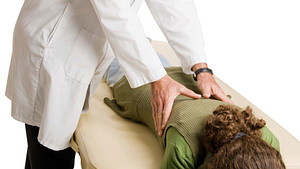 Chiropractor performing a spinal adjustment on a patient face down.
