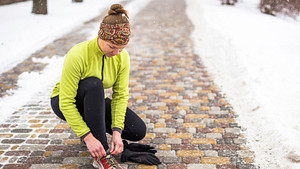 Woman tying her shoe outside on a winter run.