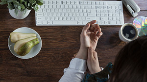 Woman&#039;s hands at a keyboard, one massaging the other