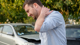 Man holding his neck and his damaged car in the background