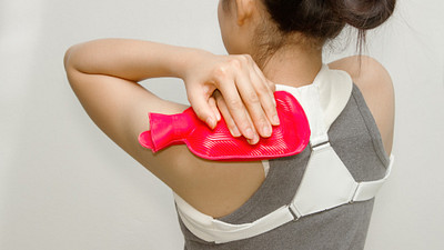 Woman applying a hot pack to her upper back