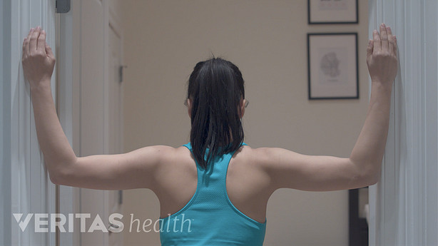 Posterior view of woman doing a corner stretch on a door frame.
