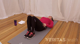 Woman lying on yoga mat doing SI Joint lumbar rotation stretch.