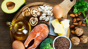 Spread of healthy foods including broccoli, salmon, eggs, olive oil, chia seeds, and avocado