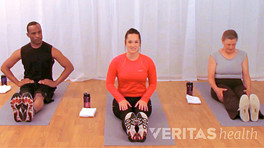 Two women and a man sitting on yoga mats in an exercise studio