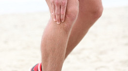 沙滩上的跑步者痛苦地抓着膝盖。