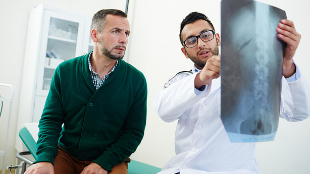 Doctor pointing to an X-ray scan, sitting next to a patient.
