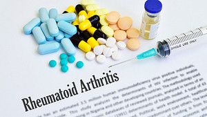 A print out of rheumatoid arthritis definition with pills and biologics laid on the tdesk