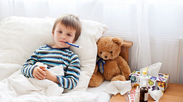 男孩在床上一个温度计和泰迪熊。
