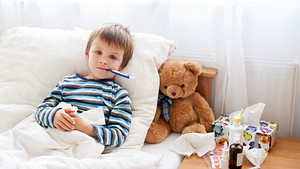 Boy in bed with a thermometer and teddy bear.