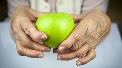 Arthritic hands holding an apple.