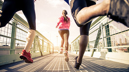 Group of three people running across a walking bridge.