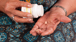 Elderly woman emptying pill from pill bottle in their hand