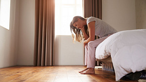 Woman sitting on the edge of the bed looking tired.