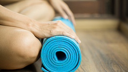 Hands resting on a rolled-up blue yoga mat