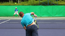 Two men playing tennis across the court from each other.