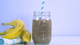 Bananas on a table top next to a blueberry mango smoothie in a mason jar.