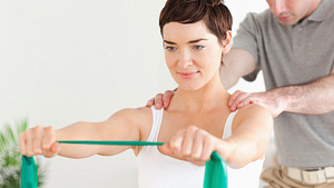 Woman working with physical therapist stretching a resistance band with both hands outstretched