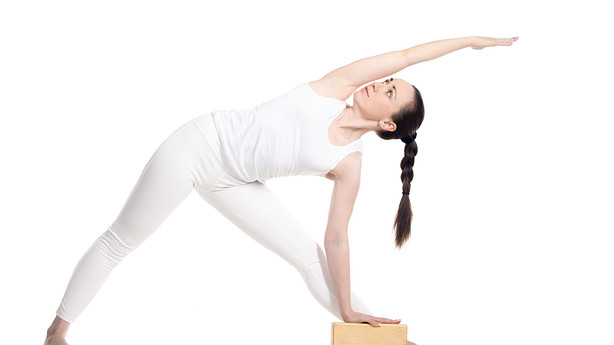 Woman performing the triangle yoga pose using a yoga block.
