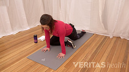 Woman pressing up on the floor with her hands with her right leg bent underneath her and her left leg stretched out behind her to stretch the piriformis muscle