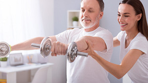 Therapist assisting patient with shoulder exercises using dumbbells.