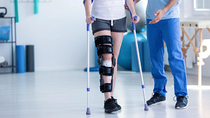 Woman walking on crutches with a knee brace in recovery.