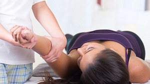 Patient lying supine on a massage table while practitioner works on the shoulder..