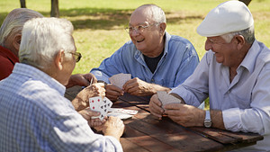 Four elderly men playing cards at a picnic table in the park