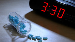 Digital clock reading 3:30 with sleeping pills scattered on the table.