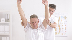 Man performing overhead shoulder exercise with physical therapist.