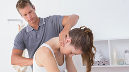 Male physical therapist examining a young woman&#039;s cervical and thoracic spine in the medical office