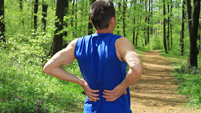 Man grasping lower back on running trail