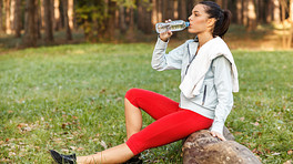 Woman sitting on a log in the forest drinking water