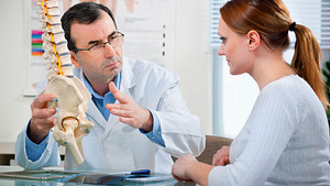 Doctor and patient having a discussion in an office while looking at a model skeleton.