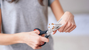 Woman cutting a bunch of cigarettes in half.