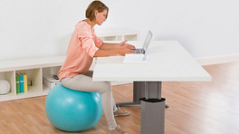 一个女人坐在她办公桌前的健身球上。