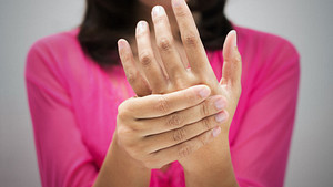 Woman wearing a pink shirt, grabbing her hands in pain.