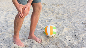 Beach volleyball player grabbing knee in pain.