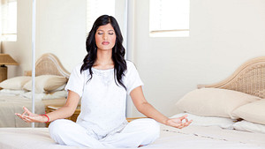 Woman sitting on bed focused in meditation.
