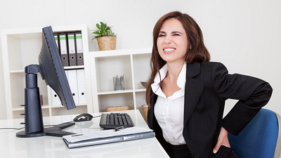 Woman grabbing her lower back while sitting at her desk.