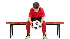 Young boy holding a soccer ball while sitting on a bench.