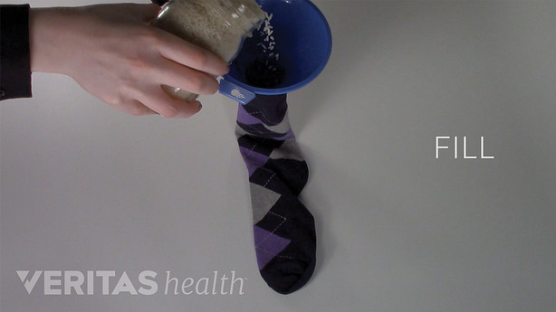Rice being poured into a sock to create a homemade heating pack. Play button overlayed to access How to Make a Moist Heat Pack Video