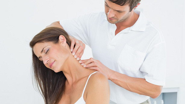 Male physical therapist massaging a young woman&#039;s neck in the medical office